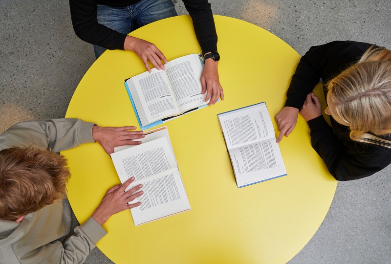 Foto som viser 3 elevar rundt eit bord i biblioteket.
